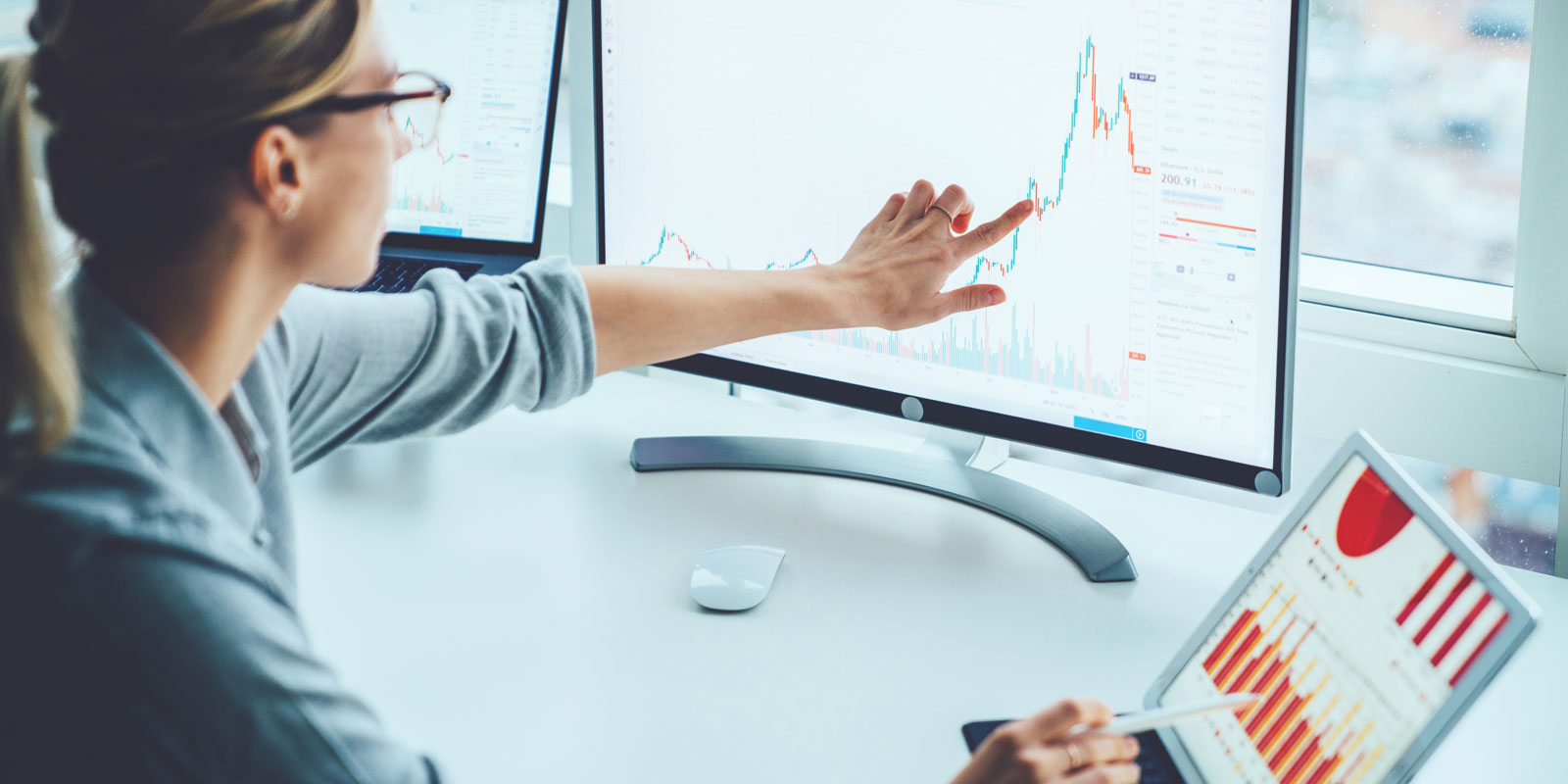 Woman pointing to charts on computer monitor.