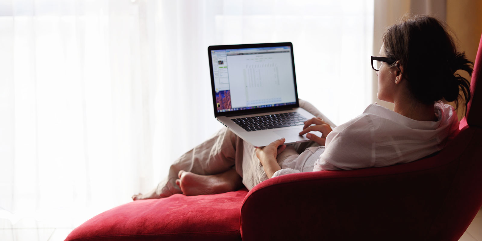 Woman sitting on red lounge chair with laptop.